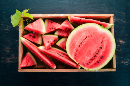 Sliced watermelon in a wooden box on a dark background - contact us for more details.