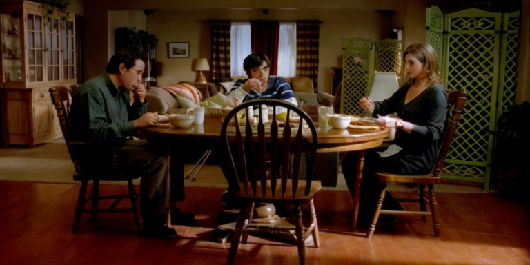 A group of people sitting around a table in a living room discussing breakfast choices.