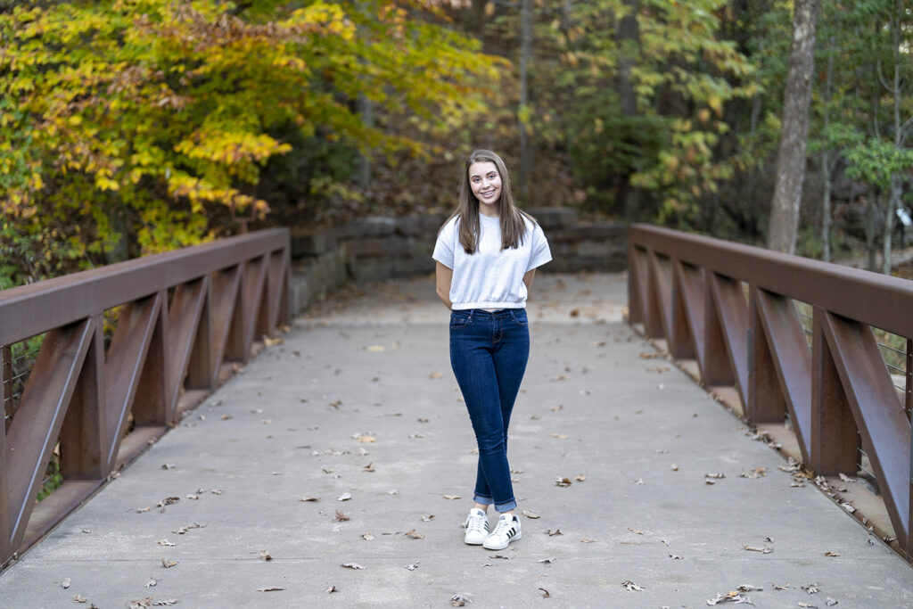 A girl standing on a bridge in the fall.