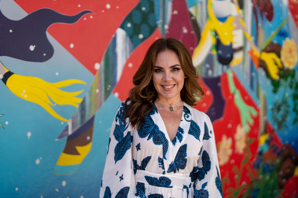 A woman standing in front of a colorful mural.