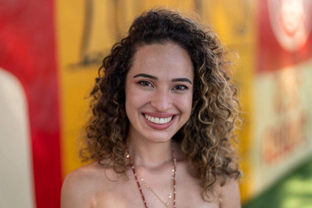 A woman with curly hair smiling in front of a colorful wall.