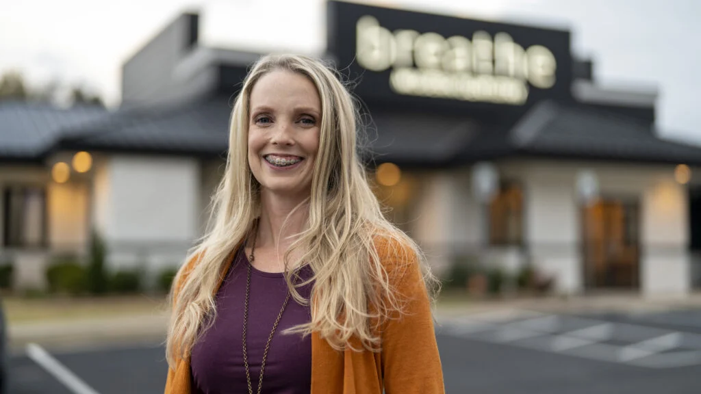 A woman smiling in front of a restaurant.