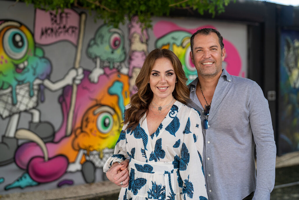 A man and woman standing in front of a graffiti covered wall.